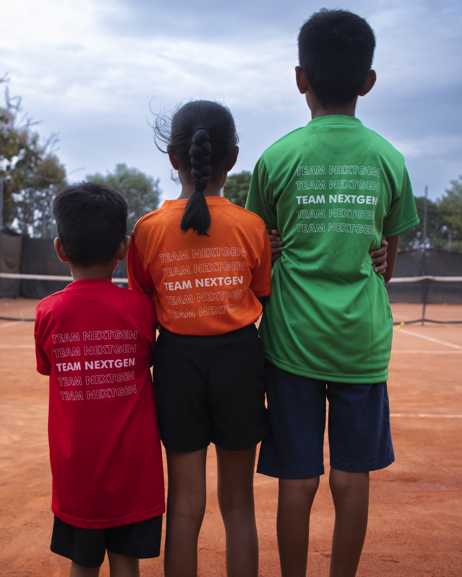 Three young Grass Roots players, arms around each other, looking out at the court